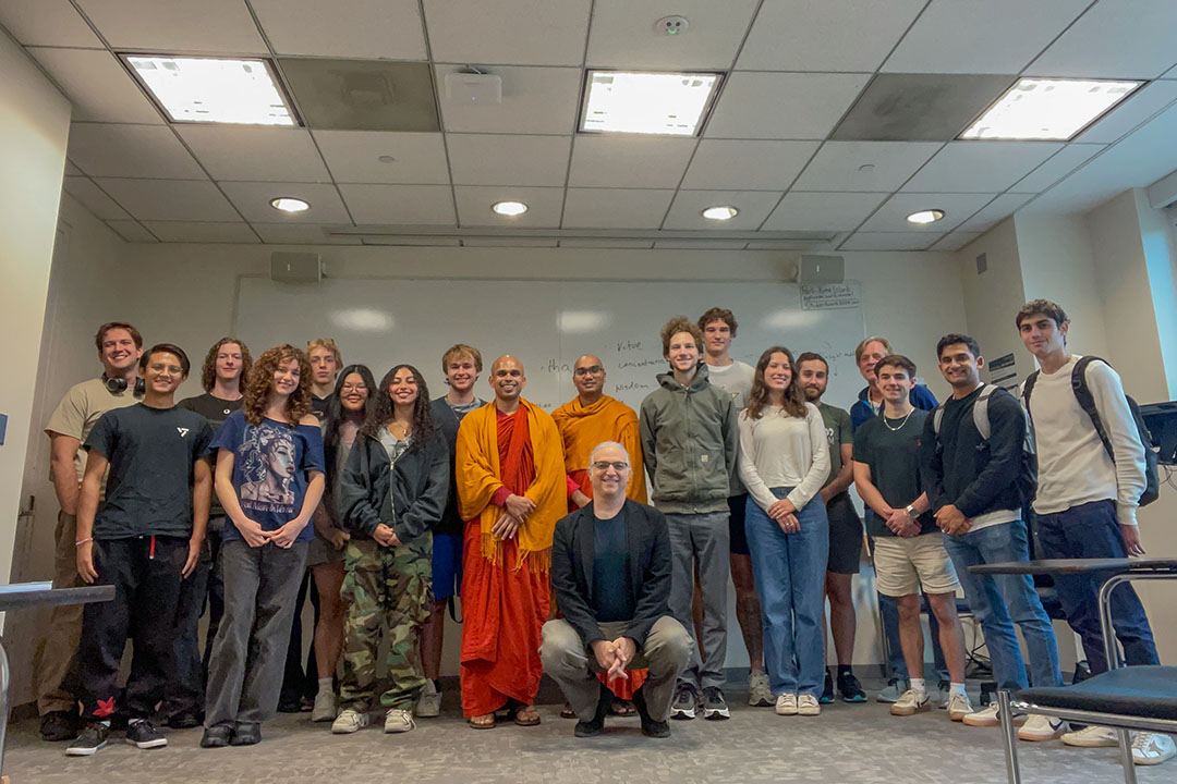 A large group of people standing gathered around a monk in orange and red robes