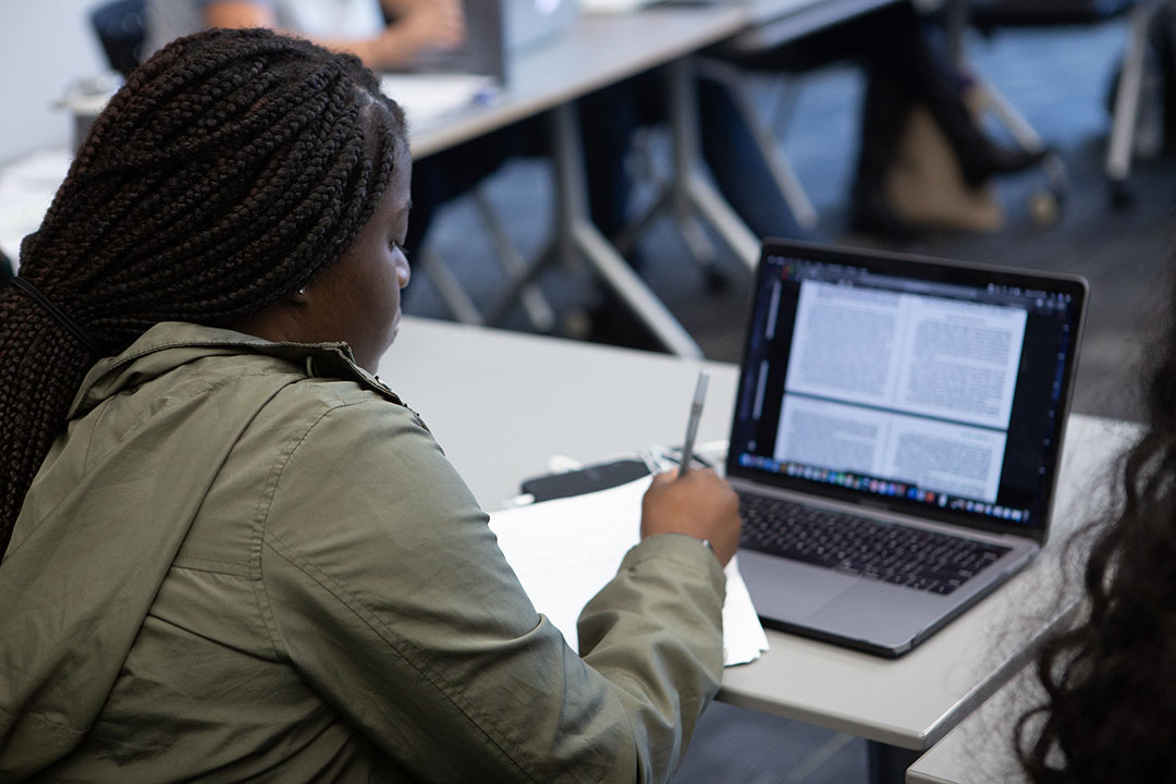 A student in class writing on a laptop and taking notes on paper