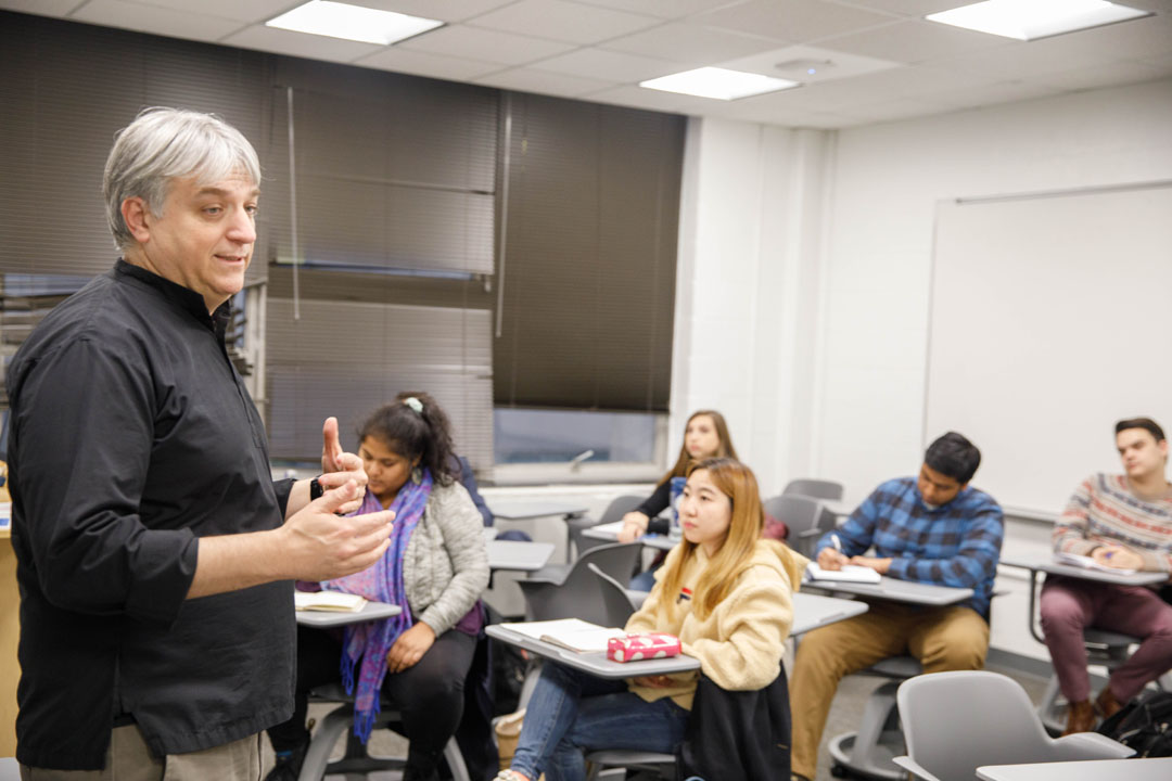 Department of World Religions text over an image of four students talking in a GW building, with the CCAS college seal watermark