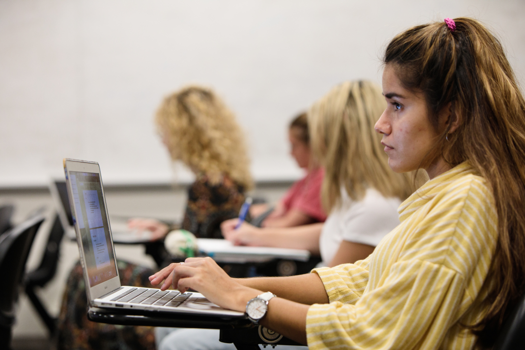 A student in profile sitting at a desk and typing at a computer in class