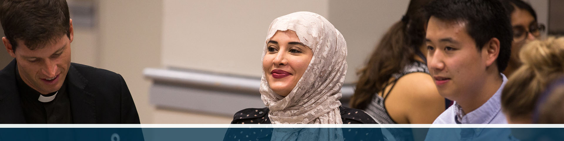 Three students sit together, one wearing a Catholic priest's collar and one wearing a head scarf.