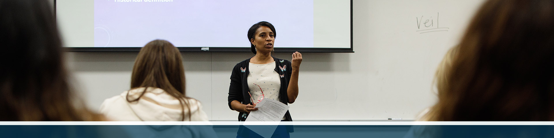 Professor Kelly Pemberton teaching a Women in Islam class in front of a projector reading "Islamic Mysticism: primordial definition, historical definition."
