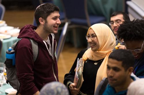 Two students, one wearing a yarmulke and one wearing a scarf, talking and smiling